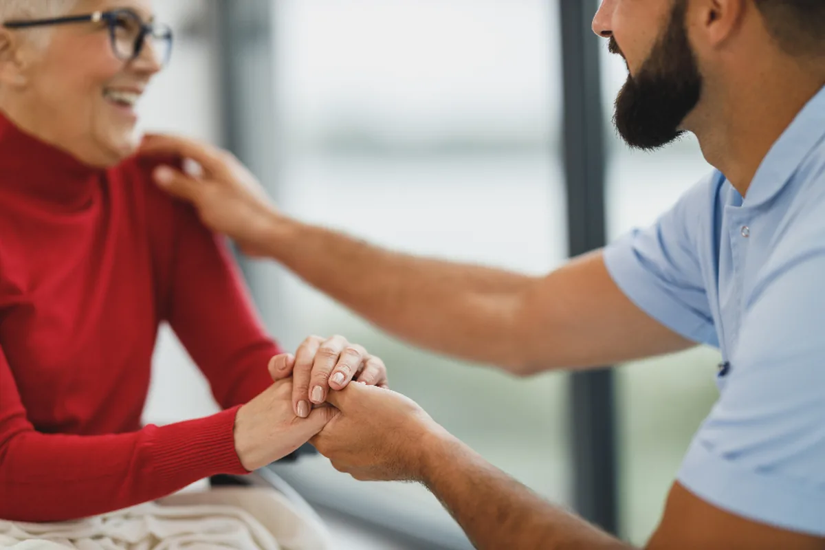 A caregiver holding an older woman's hand, both smiling